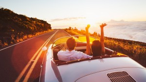 Happy couple driving on country road into sunset
