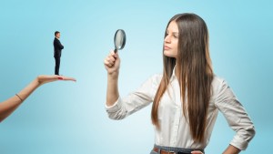 Young woman looking at tiny man with magnifying glass