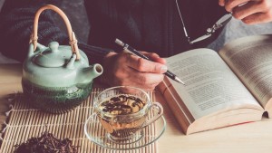 Man reading a book with cup of tea and tea pot
