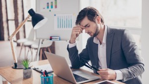 Young man sitting at desk holding head